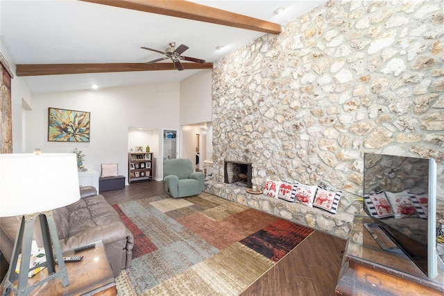 living area featuring a stone fireplace, beam ceiling, wood finished floors, and a ceiling fan