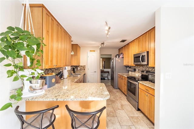 kitchen featuring tasteful backsplash, appliances with stainless steel finishes, a peninsula, light stone countertops, and a sink