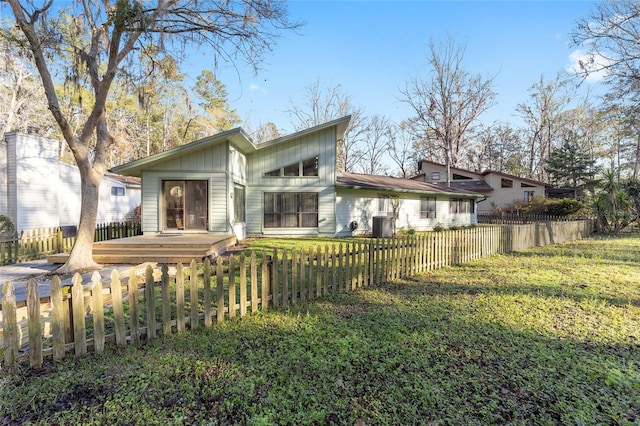 rear view of house featuring board and batten siding, a yard, a fenced front yard, and central air condition unit