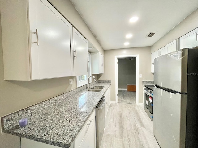 kitchen with light wood-style flooring, appliances with stainless steel finishes, light stone counters, white cabinetry, and a sink