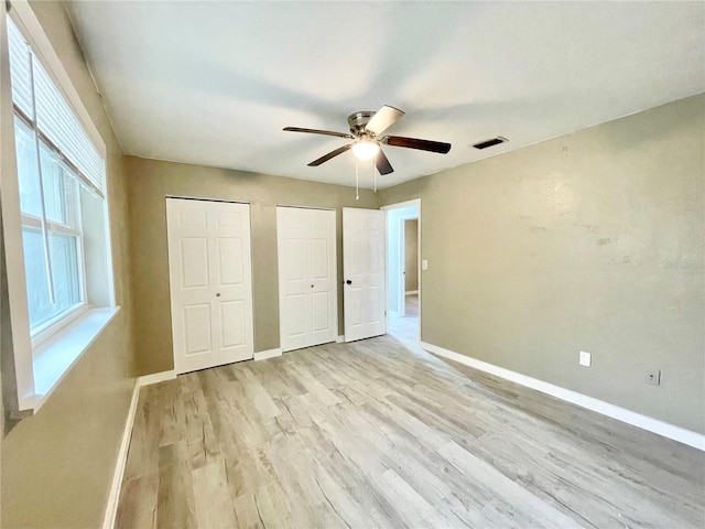 unfurnished bedroom with multiple closets, visible vents, light wood-style floors, and baseboards