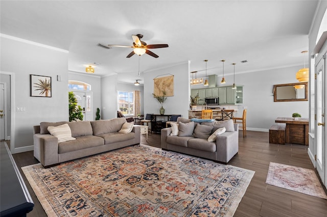 living area featuring ceiling fan, visible vents, baseboards, dark wood-style floors, and crown molding