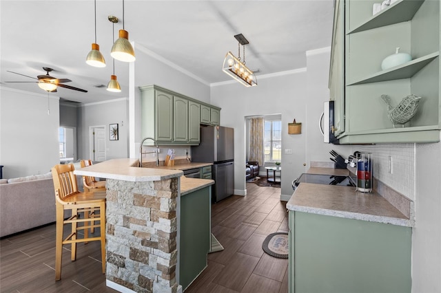 kitchen featuring a peninsula, stainless steel appliances, wood finish floors, a kitchen breakfast bar, and green cabinetry