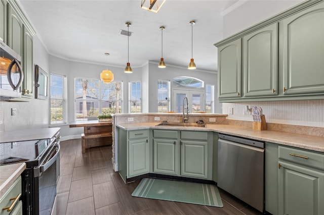 kitchen featuring a peninsula, a sink, green cabinets, light countertops, and appliances with stainless steel finishes