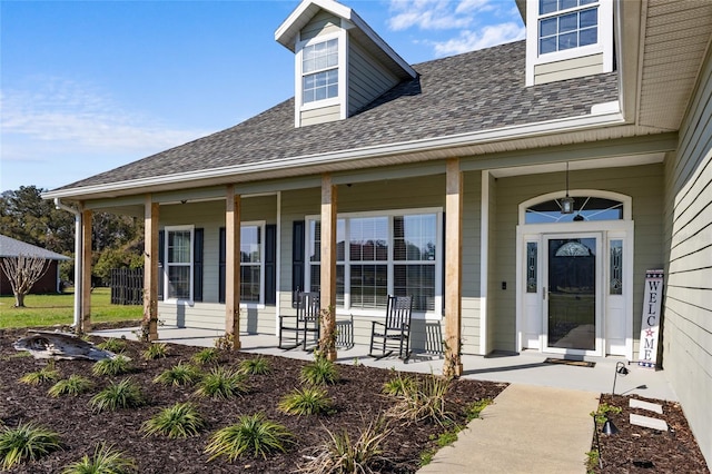 doorway to property featuring covered porch and a shingled roof