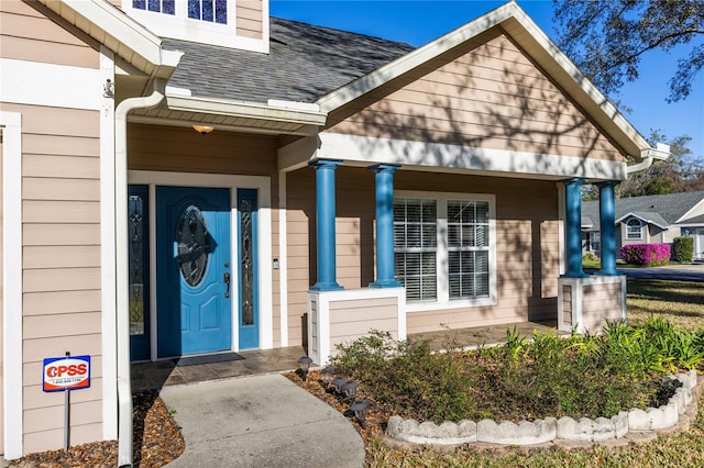 doorway to property with a porch and a shingled roof