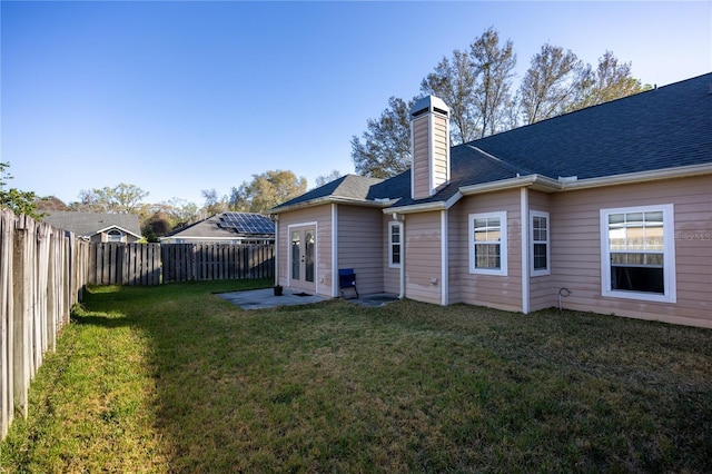 rear view of property featuring roof with shingles, a fenced backyard, a chimney, french doors, and a lawn