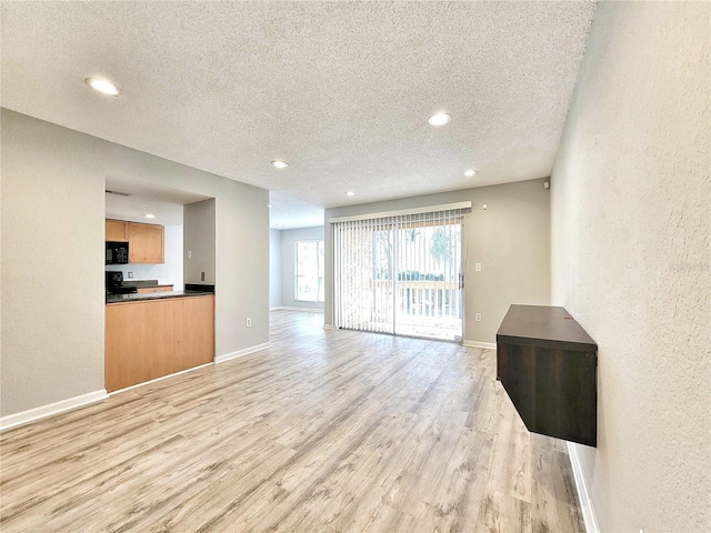 living room featuring a textured wall, light wood-style flooring, baseboards, and a textured ceiling