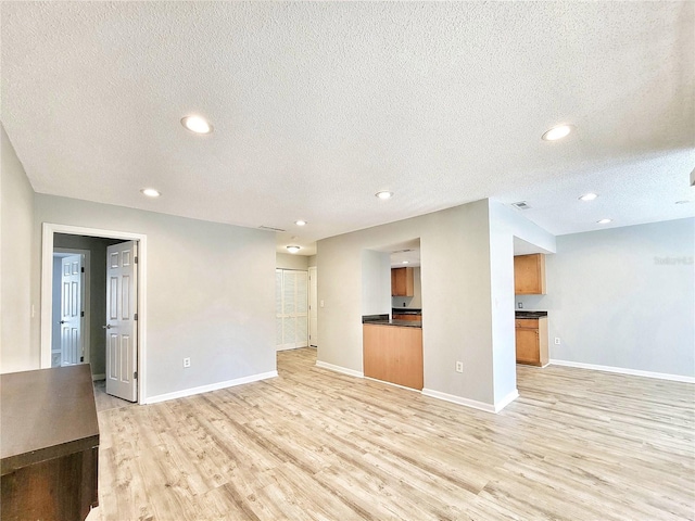 unfurnished living room with light wood-style flooring, baseboards, a textured ceiling, and recessed lighting