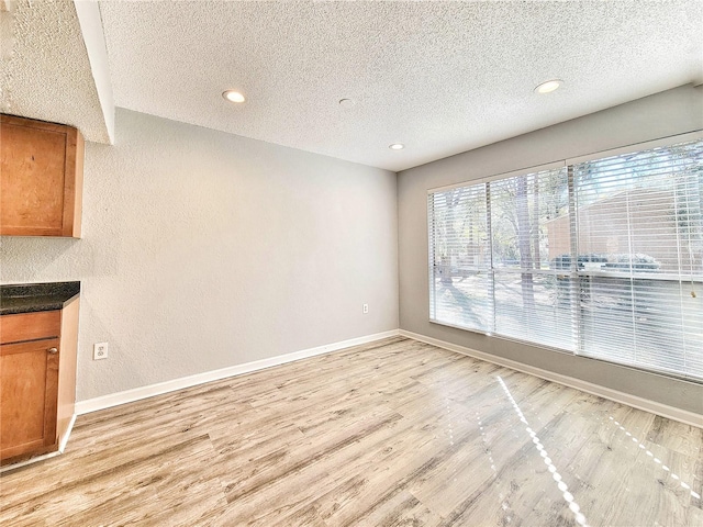 interior space with light wood finished floors, baseboards, and a textured ceiling