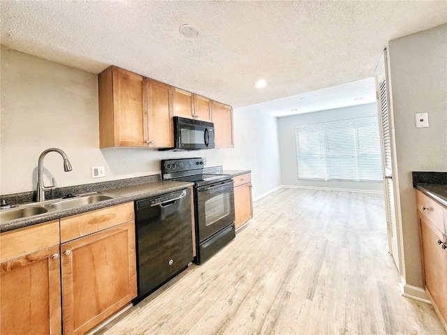 kitchen featuring a textured ceiling, a sink, light wood-style floors, black appliances, and dark countertops