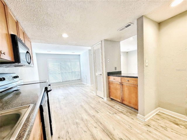 kitchen with visible vents, brown cabinetry, a textured ceiling, light wood-type flooring, and black microwave