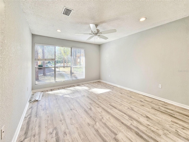 spare room featuring a textured wall, wood finished floors, visible vents, and baseboards