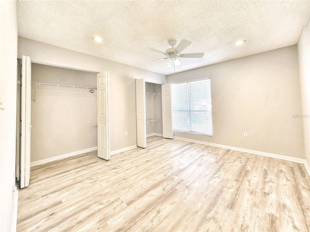 unfurnished bedroom with wood finished floors, a textured ceiling, baseboards, and two closets