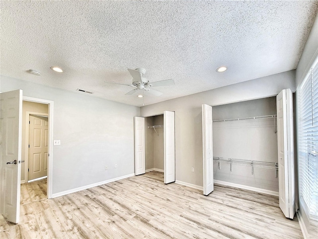 unfurnished bedroom with a textured ceiling, visible vents, baseboards, light wood-type flooring, and two closets