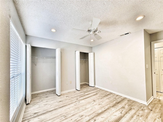 unfurnished bedroom featuring light wood-style floors, baseboards, visible vents, and multiple closets