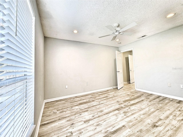 unfurnished room featuring visible vents, light wood-style floors, a ceiling fan, a textured ceiling, and baseboards