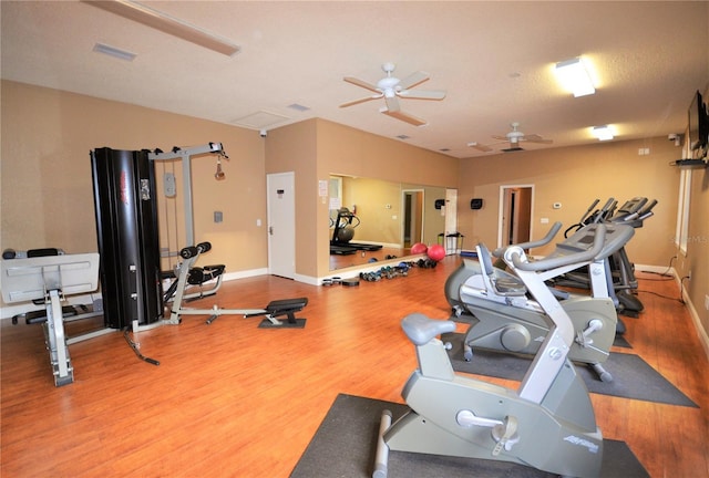 gym with baseboards, visible vents, a ceiling fan, and wood finished floors