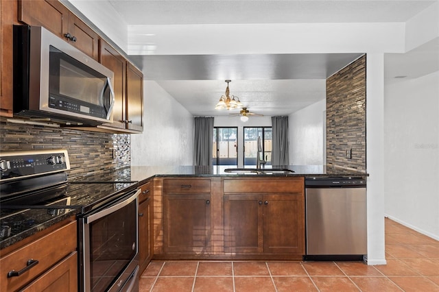 kitchen with light tile patterned floors, a sink, appliances with stainless steel finishes, tasteful backsplash, and dark stone countertops