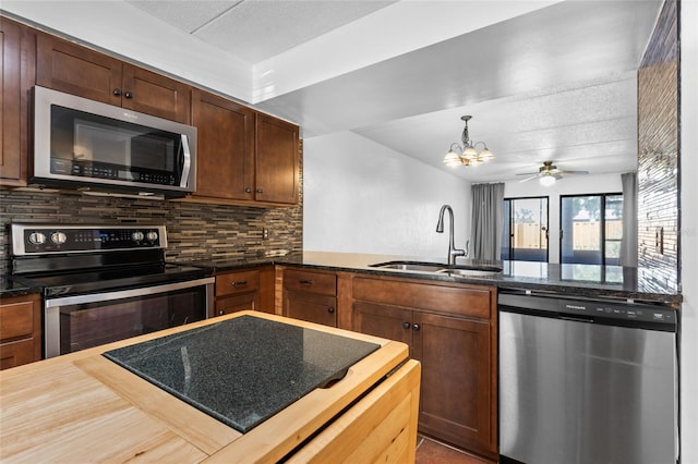 kitchen featuring a peninsula, a sink, appliances with stainless steel finishes, backsplash, and dark stone counters