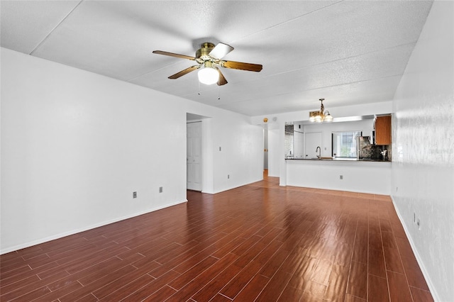 unfurnished living room with dark wood-style flooring, a sink, baseboards, and ceiling fan with notable chandelier