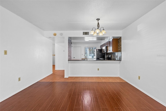 unfurnished living room with a chandelier, a sink, wood finished floors, visible vents, and baseboards