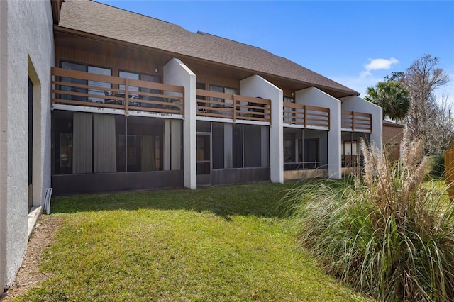 rear view of house featuring a yard, a shingled roof, and stucco siding