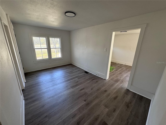 spare room featuring visible vents, baseboards, dark wood finished floors, and a textured ceiling