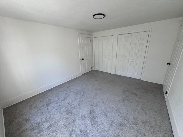 unfurnished bedroom featuring carpet, a textured ceiling, baseboards, and two closets