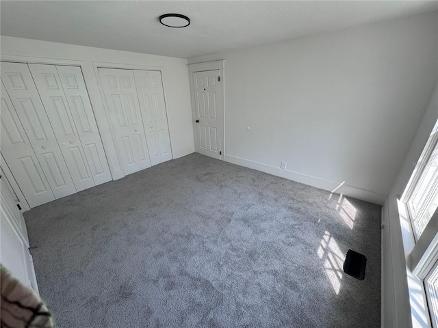 unfurnished bedroom with carpet, two closets, and baseboards