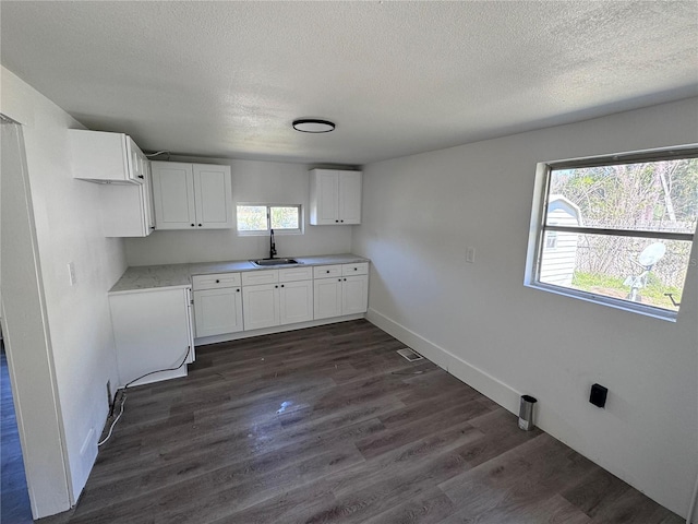 kitchen with a sink, white cabinetry, baseboards, light countertops, and dark wood finished floors