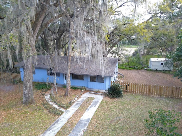 view of front of home with concrete driveway, roof with shingles, fence, and a front lawn