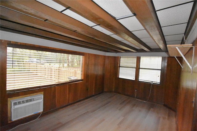 unfurnished room featuring an AC wall unit, a drop ceiling, light wood-type flooring, and wooden walls