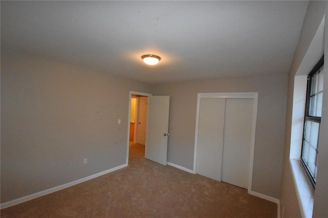 unfurnished bedroom with baseboards, a closet, and light colored carpet