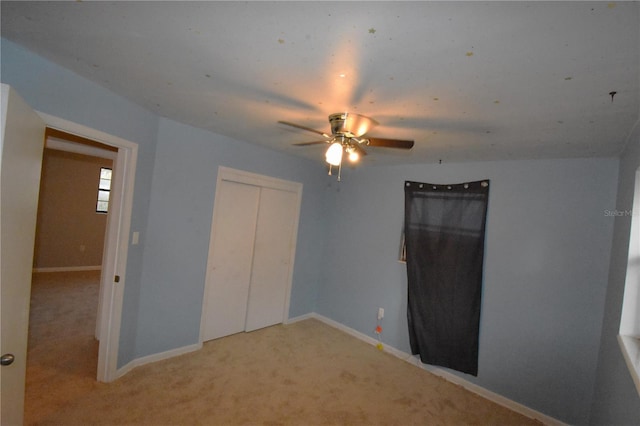 unfurnished bedroom featuring a ceiling fan, a closet, light carpet, and baseboards