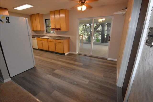 kitchen with dark wood finished floors, light brown cabinets, a sink, white appliances, and baseboards