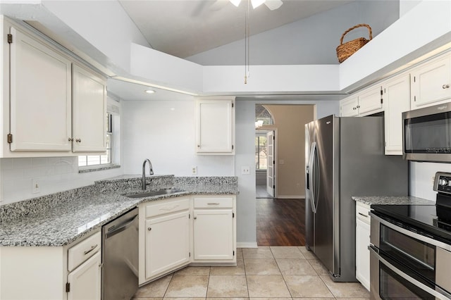 kitchen featuring decorative backsplash, lofted ceiling, appliances with stainless steel finishes, light stone countertops, and a sink