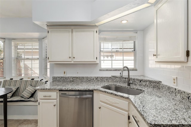 kitchen featuring light tile patterned floors, a sink, stainless steel dishwasher, decorative backsplash, and light stone countertops