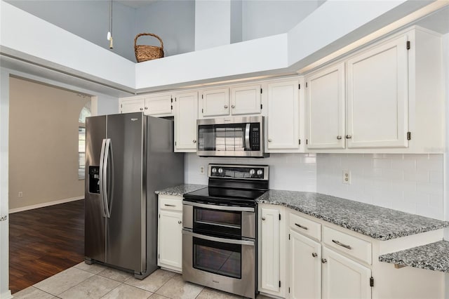 kitchen featuring light tile patterned floors, stainless steel appliances, tasteful backsplash, white cabinetry, and dark stone countertops