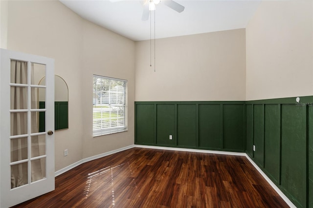 unfurnished room with dark wood-type flooring, wainscoting, a decorative wall, and a ceiling fan