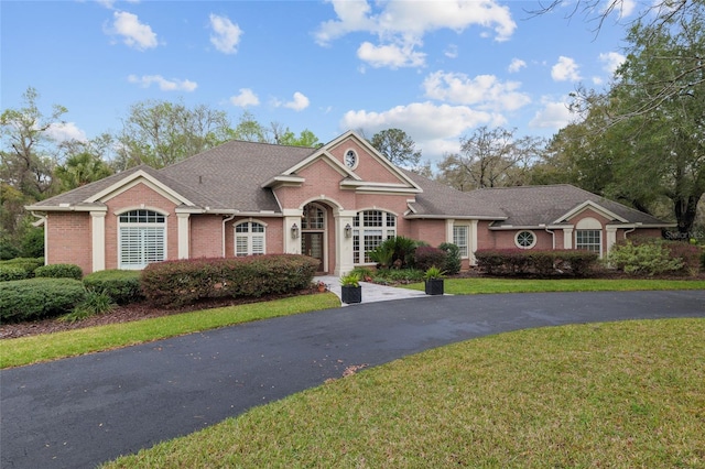 view of front facade featuring driveway, brick siding, roof with shingles, and a front yard