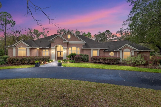 view of front of home featuring aphalt driveway, a lawn, and brick siding