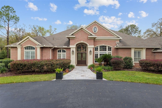 view of front of house with french doors, brick siding, and roof with shingles