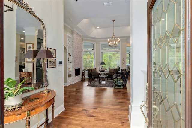 entryway featuring baseboards, a chandelier, ornamental molding, a fireplace, and wood finished floors