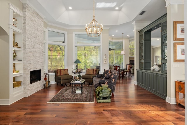 living area featuring built in shelves, dark wood finished floors, an inviting chandelier, a fireplace, and crown molding