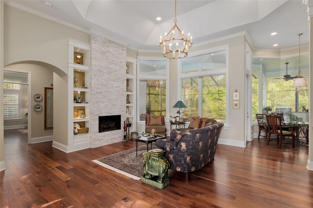 living room featuring built in features, dark wood finished floors, arched walkways, a stone fireplace, and baseboards