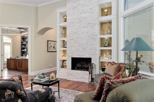 living room with baseboards, built in features, ornamental molding, a fireplace, and wood finished floors