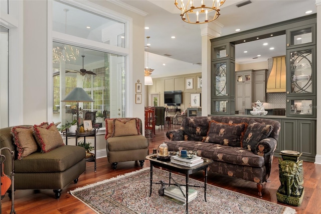 living area featuring ceiling fan with notable chandelier, wood finished floors, visible vents, and ornamental molding