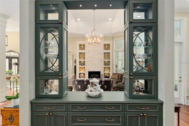 bar with built in shelves, wood finished floors, a large fireplace, crown molding, and hanging light fixtures