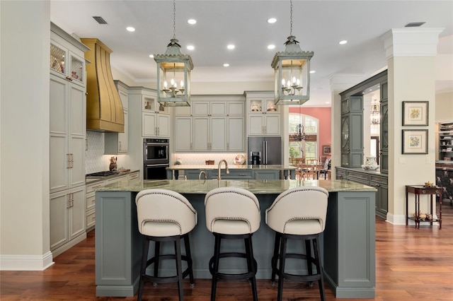 kitchen featuring premium range hood, visible vents, refrigerator with ice dispenser, a large island with sink, and dark wood-style flooring